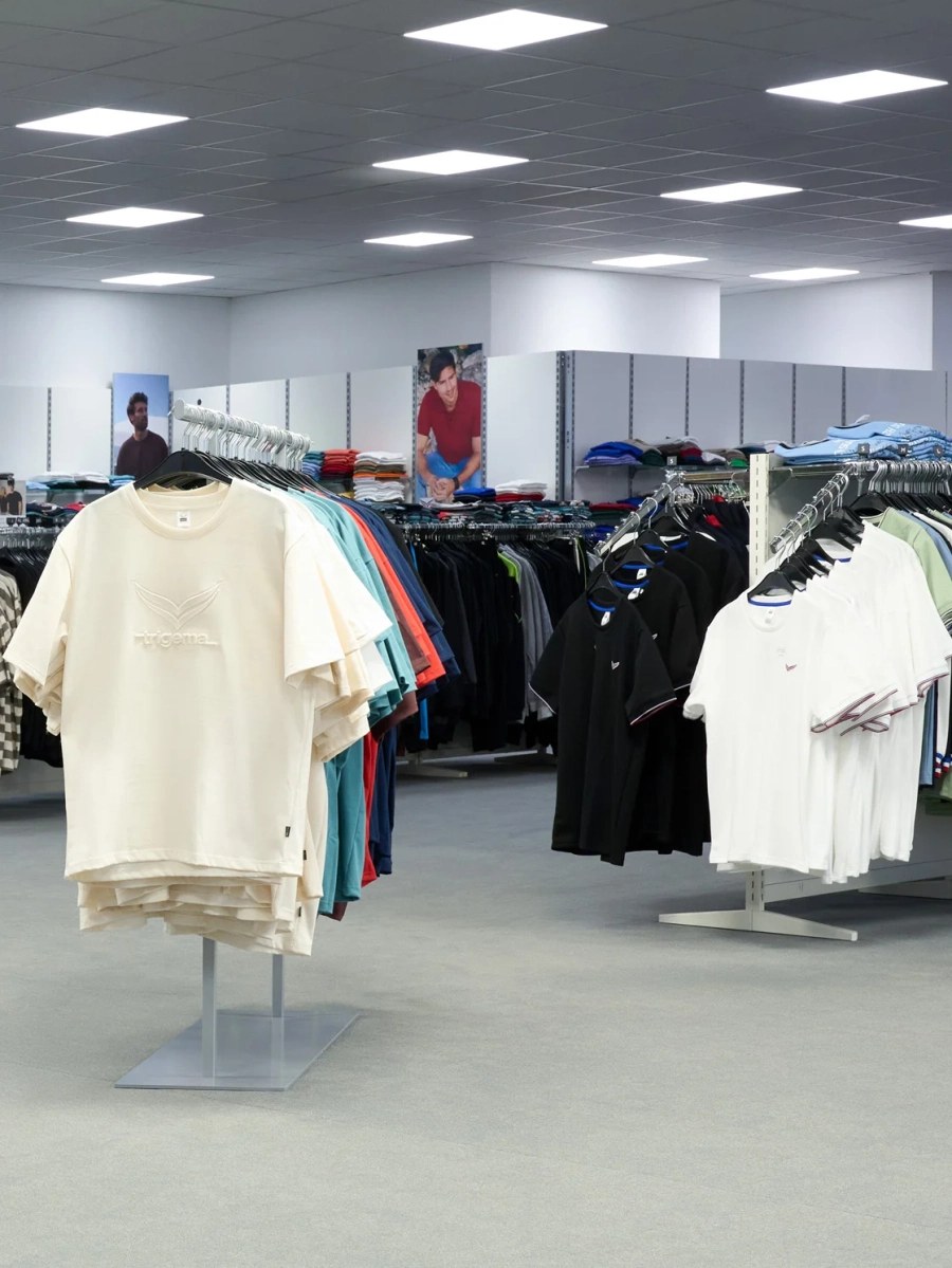 Blick in ein Trigema-Testgeschäft mit Shirts und Poloshirts auf Kleiderständern